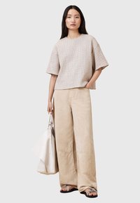 Top beige a maniche corte con texture e motivo a pois; abbinato a pantaloni larghi di colore chiaro; porta una borsa bianca; sandali flat.