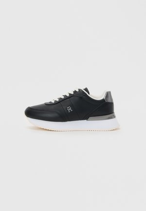 Black leather sneaker with white sole, featuring a rounded toe, lace-up front, and subtle metallic accent at the heel.