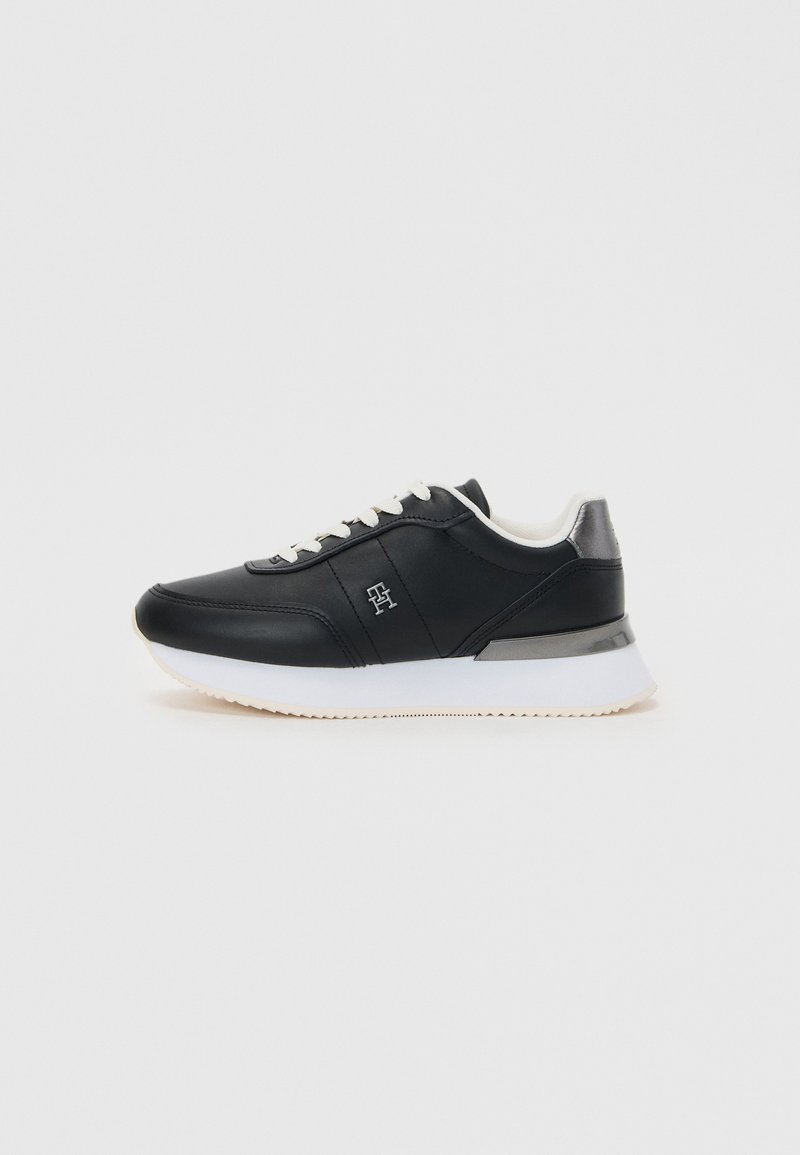 Black leather sneaker with white sole, featuring a rounded toe, lace-up front, and subtle metallic accent at the heel.