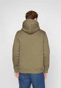 Felpa con cappuccio verde oliva, dotata di tasca a marsupio, polsini e orlo a costine; realizzata in un morbido tessuto testurizzato. Design semplice e funzionale.