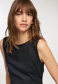 Top senza maniche a righe nere con scollatura rotonda, caratterizzato da un tessuto leggermente texturizzato e una tasca con cucitura sul lato sinistro.