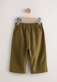 Shorts vert kaki en tissu texturé, dotés d'une taille élastique et d'une coupe à jambes larges, suspendus à une pince en bois.