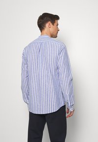 Striped shirt in blue and white, featuring long sleeves, a button-down collar, and a relaxed fit. Back has a yoke detail and side slits.