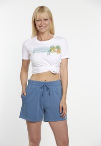 Hvid knyttet T-shirt med et farverigt frugt- og bladgrafik, parret med blå sportsshorts med elastisk talje og lommer.