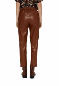 Bruine leren tapered broeken met een elastische tailleband, voorzien van twee achterzakken en een gladde textuur, gecombineerd met zwarte laarzen.