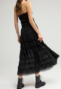 Jupe maxi noire à volants en tulle transparent, comportant des couches froncées, associée à un haut noir ajusté et des bottes de combat noires à lacets.