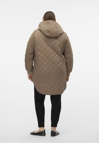 Veste longue matelassée beige avec une capuche, présentant un motif en losanges et des poignets côtelés, associée à un pantalon noir slim et des ballerines noires.