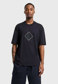 T-shirt nero a maniche corte con una grafica a diamante a contrasto al centro e dettagli texture sulle spalle. Materiale morbido con una vestibilità rilassata.