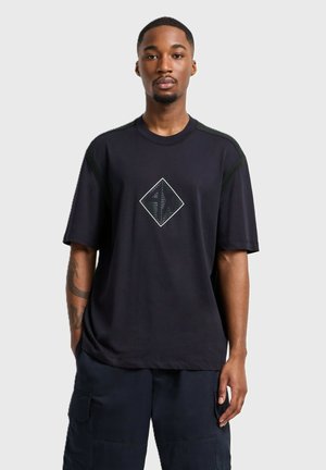 T-shirt nero a maniche corte con una grafica a diamante a contrasto al centro e dettagli texture sulle spalle. Materiale morbido con una vestibilità rilassata.
