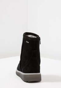 Černá semišová zimní bota s šedou gumovou podrážkou a viditelnou fleece podšívkou, z pohledu zezadu na bílém povrchu.