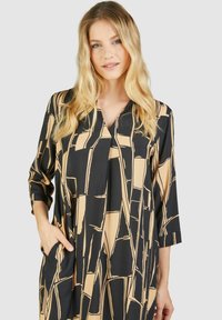 Schwarz-beige gemustertes Kleid mit V-Ausschnitt, Dreiviertelärmeln und seitlichen Taschen; aus leichtem Stoff mit glatter Textur gefertigt.