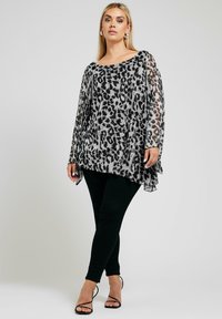 Transparent, lätt svart och grå leopardmönstrad topp med vid halsringning och flödig silhuett, kombinerad med svarta tajta byxor och sandaletter med remmar.