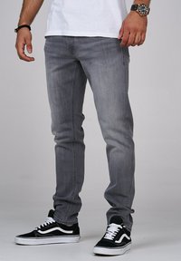 Jeans in denim grigio con una vestibilità slim, caratterizzati da dettagli di cucitura discreti, abbinati a sneaker bianco e nero.