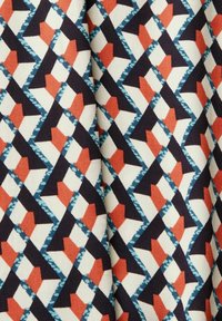 Geometric fabric pattern in cream, navy, red, and teal. Features zigzag and triangular shapes with contrast stitching details.