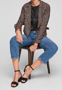 En tweedblazer i svart, vitt och rött med en figursydd design; matchad med högmidjade blå cropped jeans och svarta remsandaler.