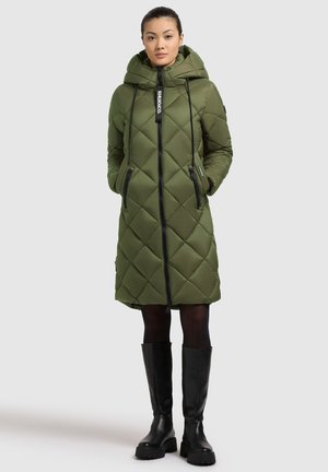 Manteau matelassé en olive avec capuche, fermeture éclair à l'avant et poches latérales. Présente des accents noirs et un design jusqu'aux genoux. Bottes noires jusqu'aux genoux.