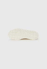 Sole of a sneaker, textured with a grid pattern, featuring the embossed word "HUGO" in the center, colored in off-white with raised edges.