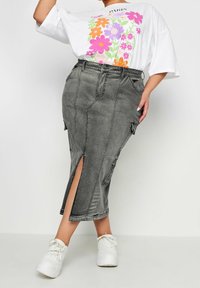 Grå denim cargokjol med sidslitsar, featuring flera fickor och en figurnära silhuett. Matchas med en vit t-shirt med grafik och vita sneakers.