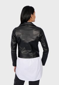 Černá kožená bunda s dlouhými rukávy a límcem, s hladkou texturou a zkráceným střihem. Nositá přes bílou košili.