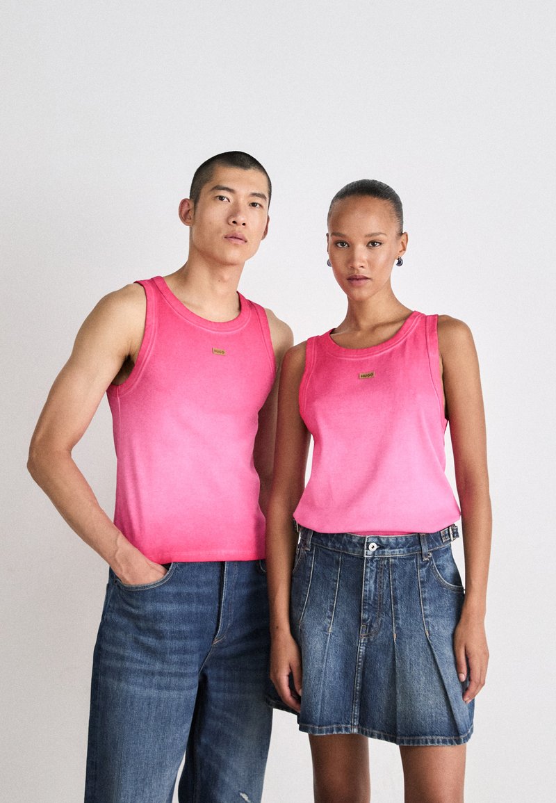 To personer har på seg matchende lys rosa ermeløse topper med gradienteffekt og logo-detaljer, sammen med denim-bukser.