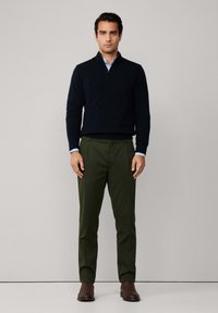 Maglione lavorato a maglia di colore blu navy con collo a zip, abbinato a pantaloni verde oliva. Stivali alla caviglia in pelle marrone completano l'outfit.