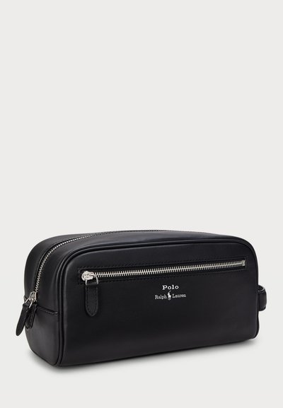 Trousse de toilette en cuir noir avec un compartiment principal zippé, une poche avant et un logo en relief. Présente une forme rectangulaire et une texture lisse.