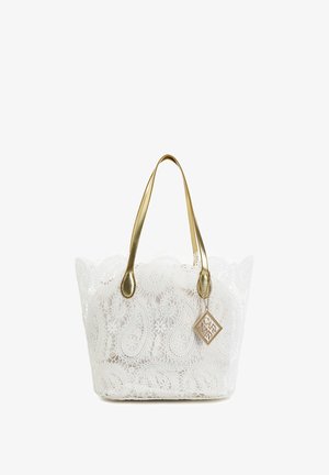 Bolso tote de encaje blanco con un elaborado patrón de paisley, asas doradas y un colgante cuadrado dorado colgando de una correa.