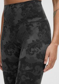 Vysoké černé legíny s texturovaným, vzorovaným designem obsahujícím odstíny šedé a jemné krajkové detaily. Hladký materiál, přiléhavý střih.