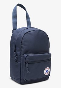 Σακίδιο πλάτης από ναυτικό ύφασμα με στρογγυλεμένο σχήμα, που διαθέτει μπροστινή τσέπη με φερμουάρ και κυκλικό λογότυπο. Έχει έναν ενιαίο ιμάντα ώμου.