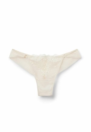 Beige thong met kant-rand en bloem borduursel op de voorkant, van zachte stof met een delicate golfrand. Heeft een zijsluiting.