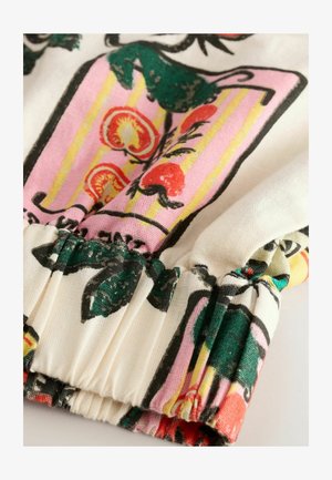 Lille taimedega kangas, millel on rohelised lehed ja punased puuviljad; kogutud mansetid tekstuuriga ja elavate värvidega.