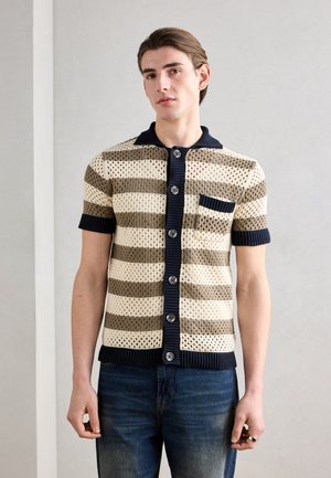 Korte ermene strikket cardigan med horisontale striper i beige og oliven, med en marineblå krage, knappelukking og en brystlomme.