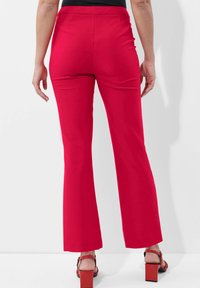 Rode uitlopende broek gemaakt van een gladde stof, met een hoge taille en een aansluitende pasvorm. Gemaakt in combinatie met sandalen met blokhak.