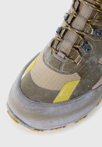 Hiking shoe featuring a mix of beige and gray materials, textured upper with yellow accents, and a rugged rubber outsole for traction.