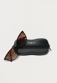 Crne mačkaste sunčane naočale s smeškanim lećama, odložene na teksturirani crni zippered etui, u kojem je utisnuta reč "vogue."
