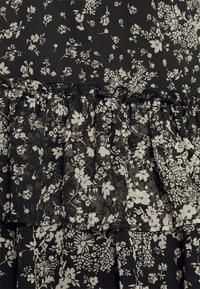 Svart tyg med vitt blommönster har en volangsträng. Texturen verkar lätt och något genomskinlig vid volangen.