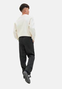 Light beige sweater with ribbed cuffs, paired with dark gray trousers featuring a back pocket. Black sneakers with white accents.