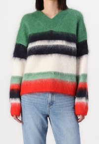 V-neck, fuzzy sweater with horizontal stripes in green, white, navy, red, and gray, paired with blue denim jeans. Soft texture evident.
