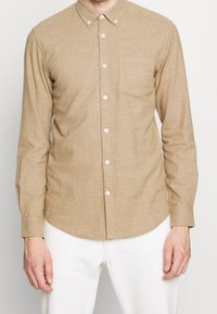Hellbraunes Hemd mit Knopfleiste aus strukturiertem Stoff. Mit spitzem Kragen, einer Brusttasche und weißen Knöpfen. Lange Ärmel.