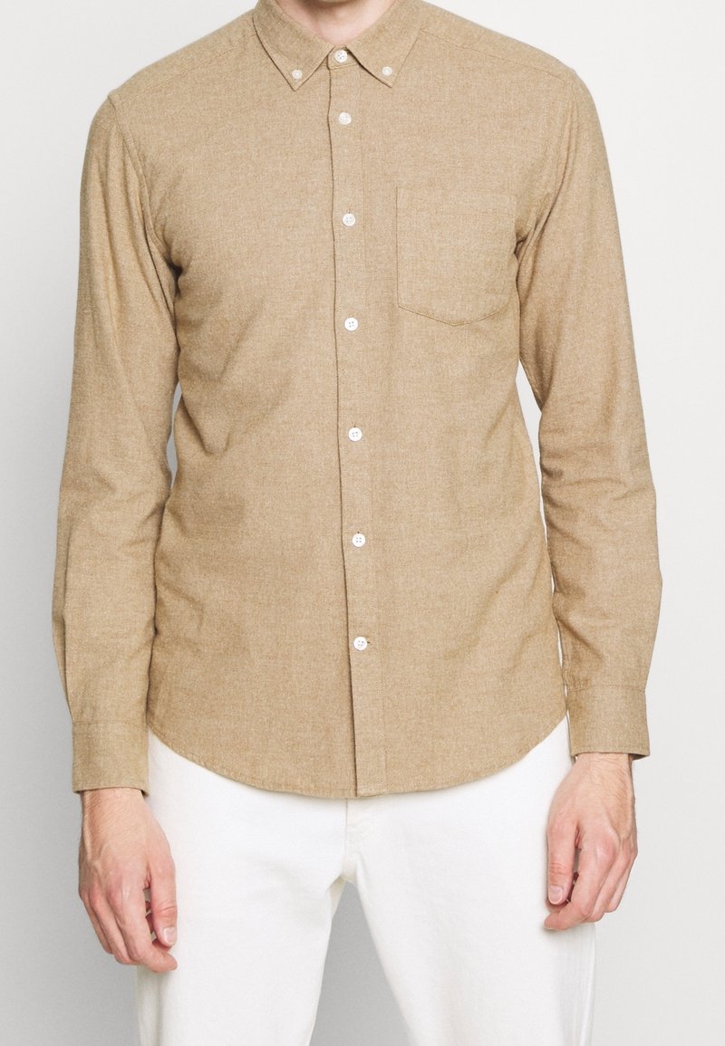 Hellbraunes Hemd mit Knopfleiste aus strukturiertem Stoff. Mit spitzem Kragen, einer Brusttasche und weißen Knöpfen. Lange Ärmel.