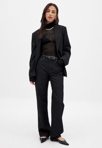 Must küllastunud püstiga bleiser, mille all on läbipaistev must pikkade varrukatega pluus, kombineeritud kõrge vöökohtadega mustade laiade pükstega ja terava nina jalanõudega. Hõbedased ketid kaunistavad.