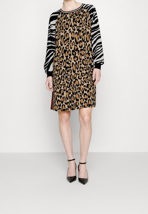 Kvinde iført en knælang kjole med leopardmønstret krop og sort-hvide zebramønstrede lange ærmer, kombineret med sorte ankelremssko.