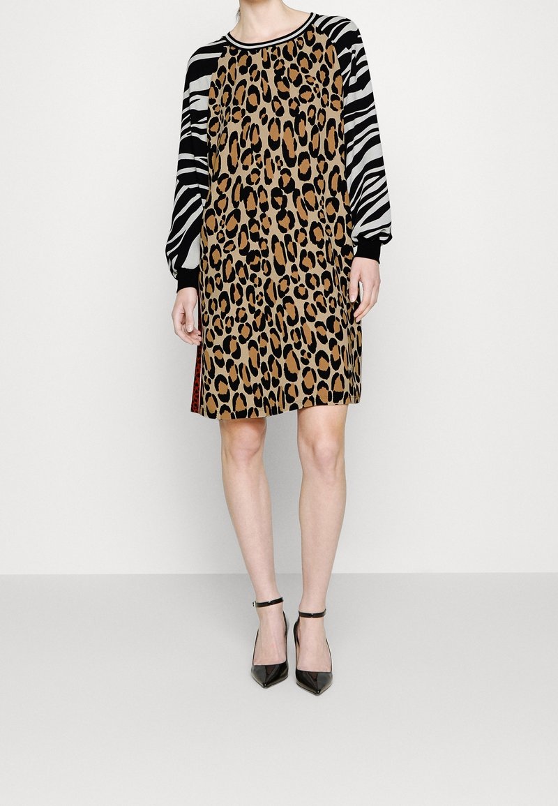 Femme portant une robe mi-longue avec un corps imprimé léopard et des manches longues à imprimé zèbre noir et blanc, associée à des talons à bride à la cheville noirs.