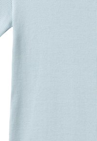 Tissu tricoté côtelé bleu clair avec une manche longue visible sur le côté gauche, montrant la texture et de fines lignes verticales.