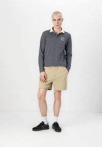 Siva polo s dolgimi rokavi s kremasto ovratnico in logotipom, v kombinaciji s bež kratkimi hlačami. Črne čevlje z belimi detajli. Enostavna, casual obleka.
