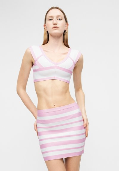Γυναίκα που φοράει στενό ροζ και λευκό ριγέ κοντό τοπ και ταιριαστή φούστα με ψηλή μέση, στέκεται με τα χέρια κοντά στους γοφούς.