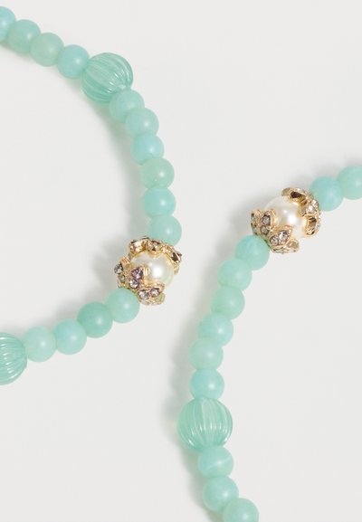 Κολιέ με ανοιχτό μπλε χάντρες που διαθέτει χρυσούς λουλουδάτους συνδέσμους με λευκές πέρλες και μικρούς διάφανους στρας σε λευκό φόντο.