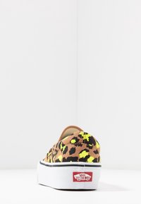 Scarpa slip-on con stampa leopardata, base marrone, accenti gialli, suola bianca e rifiniture nere. Presenta la patch del logo Vans sul tallone.