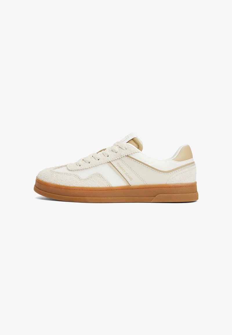 Beige sneakers with a suede and synthetic upper, featuring a perforated toe, flat lace closure, and a textured rubber sole.
