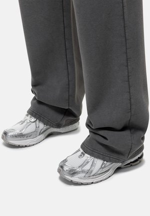 Grijze sweatpants in combinatie met metallic zilveren sport schoenen. De schoenen hebben een mesh ontwerp en textuurelementen, wat een sportieve uitstraling benadrukt.